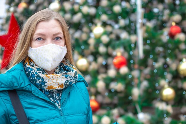 Una mujer con una máscara protectora cerca de un árbol de Navidad decorado festivamente en la calle. Navidad y año nuevo durante la pandemia de coronavirus.