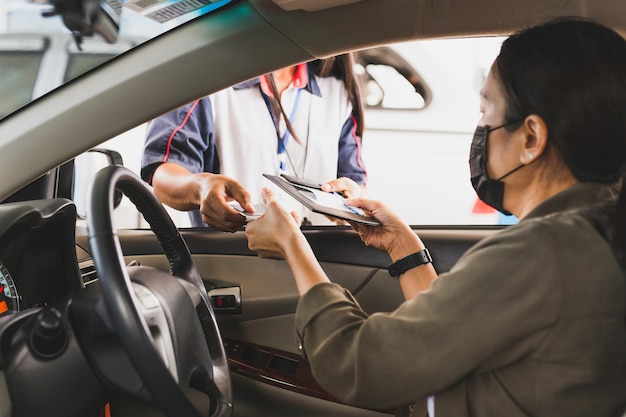 Mujer con máscara protectora en un coche pagando gasolina con tarjeta de crédito en la gasolinera.