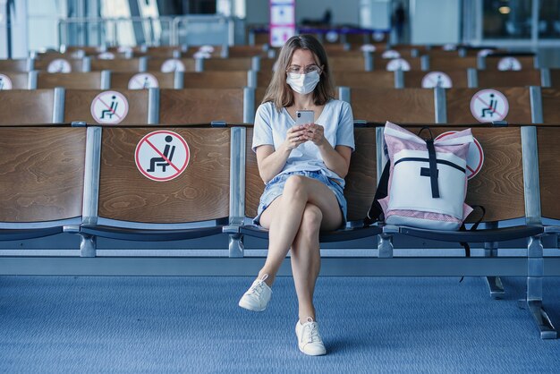 Mujer con máscara protectora esperando el avión en el aeropuerto hermosa chica usa teléfono móvil en