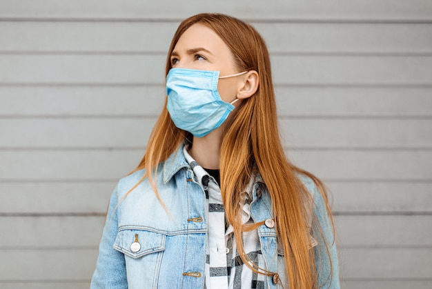 Mujer en una máscara protectora médica de pie contra una pared gris