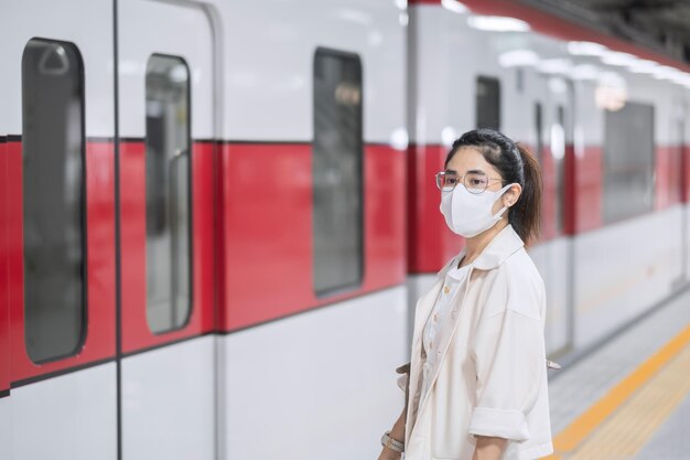 Mujer con máscara protectora para la prevención de la inflexión del coronavirus durante la espera del tren. transporte público. distanciamiento social, nueva normalidad y seguridad bajo la pandemia del covid-19