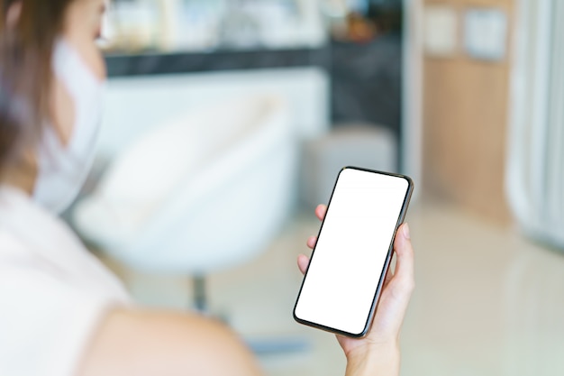 Mujer con máscara protectora que muestra la pantalla en blanco del teléfono inteligente.