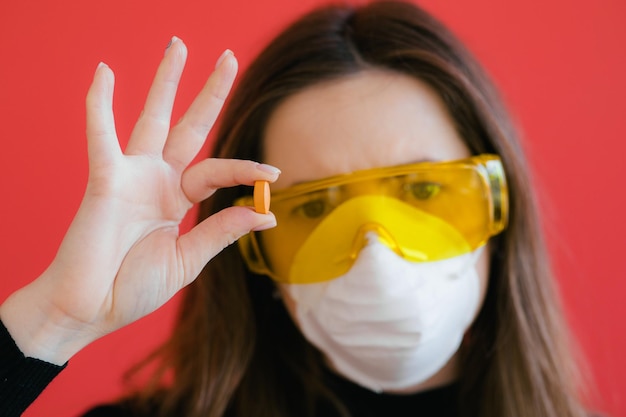 Foto mujer con máscara protectora sostenga la píldora médica en la mano sobre fondo rojo.