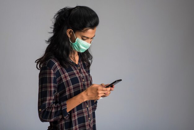 Mujer con una máscara quirúrgica utilizando un teléfono inteligente para la comunicación. Trabajar desde casa concepto.