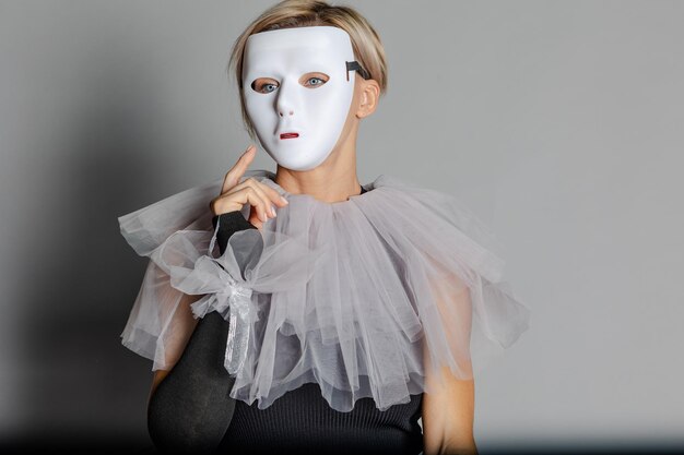Mujer con máscara de teatro blanca y collar de arlequín sobre fondo gris