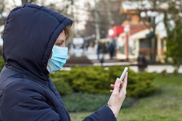 Mujer con mascarilla durante el brote de coronavirus y mantiene en la mano un smarphone