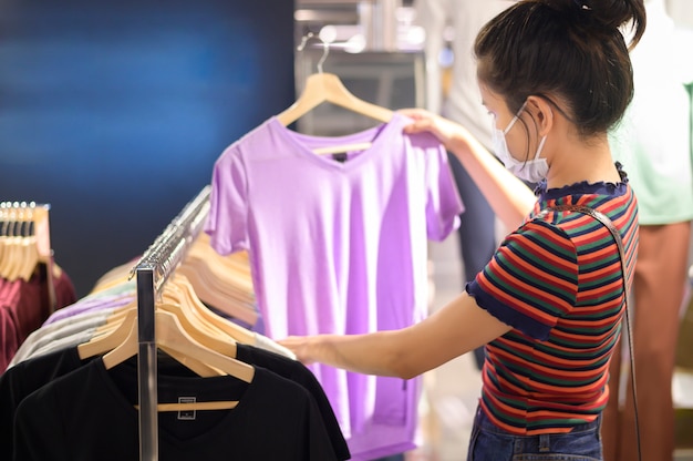 Mujer con mascarilla es comprar ropa en el centro comercial