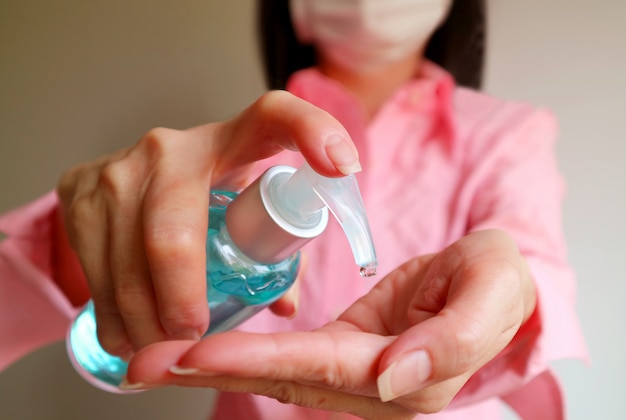 Mujer con mascarilla con gel limpiador de alcohol para frotar las manos para prevenir la infección