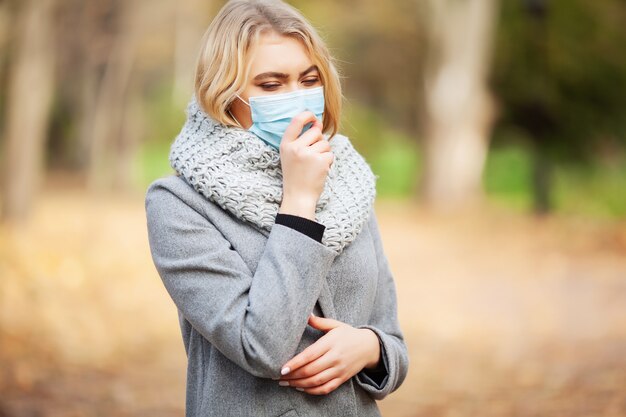 Mujer con una mascarilla médica en bosque otoñal