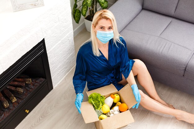 mujer con mascarilla médica Desmonta bolsas de comida en casa en la cocina. cuarentena. concepto de salud. Coronavirus. pedido de productos en línea. Entrega de productos a casa