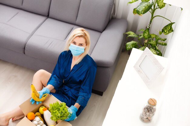 mujer con mascarilla médica Desmonta bolsas de comida en casa en la cocina. cuarentena. concepto de salud. Coronavirus. pedido de productos en línea. Entrega de productos a casa