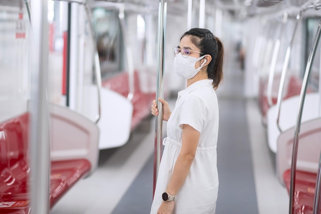 Mujer con mascarilla médica y escuchar música con auriculares en el tren. transporte público y seguridad bajo la pandemia del covid-19