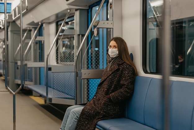 Una mujer con una mascarilla médica para evitar la propagación del coronavirus está sentada sola en un moderno vagón de metro. Una niña con una máscara quirúrgica mantiene una distancia social en un tren de metro.