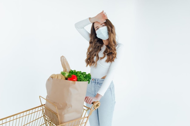 Mujer con mascarilla médica sosteniendo una bolsa de compras llena de alimentos frescos.