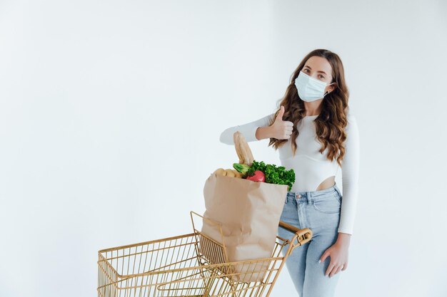 Mujer con mascarilla médica sosteniendo una bolsa de compras llena de alimentos frescos.