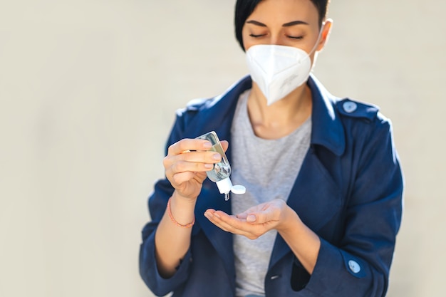 Mujer con mascarilla médica, usando un pequeño desinfectante de manos antibacteriano portátil en la calle durante el brote de Covid 19. Protección en prevención del coronavirus.