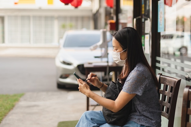 Mujer con mascarilla mediante móvil esperando comida para llevar fuera del restaurante.