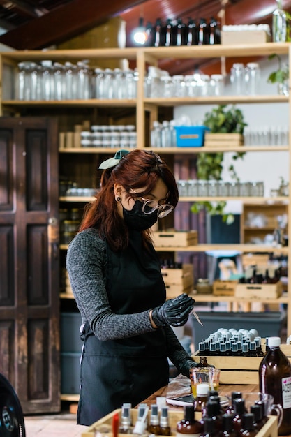 Mujer con mascarilla preparando esencias artesanales en un pequeño negocio. Producción artesanal.