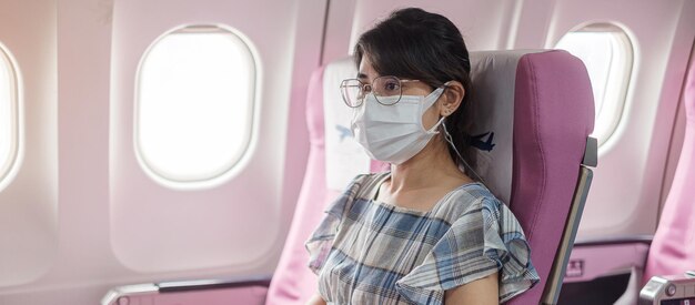 Mujer con mascarilla protectora sentada en avión o transporte público, protección contra la infección por coronavirus, turista listo para viajar. Siguiente concepto Normal, turismo y reapertura