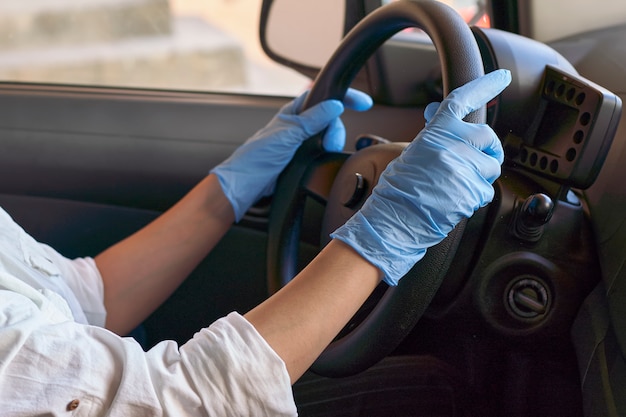 Mujer en mascarilla quirúrgica y guantes conduciendo coche