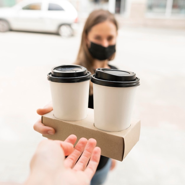 Mujer con mascarilla recibiendo café para llevar