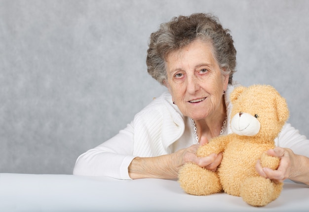 Mujer mayor entre 70 y 80 años sentada con osito de peluche en la mesa. De cerca