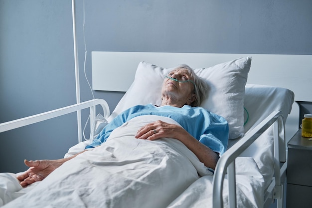 Mujer mayor acostada en la cama en la sala del hospital, siendo tratada en el hospital