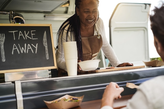 Foto mujer mayor afroamericana que sirve comida para llevar dentro del camión de comida - enfoque suave en el rostro femenino