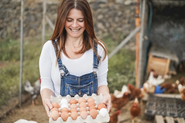 Mujer mayor agricultor recogiendo huevos orgánicos en el gallinero - Centrarse en la cara