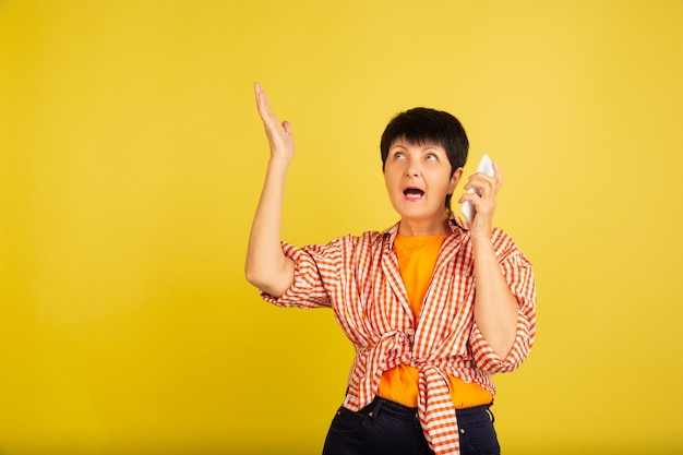 Mujer mayor aislada sobre fondo amarillo. Tecnología y concepto de estilo de vida de ancianos alegre