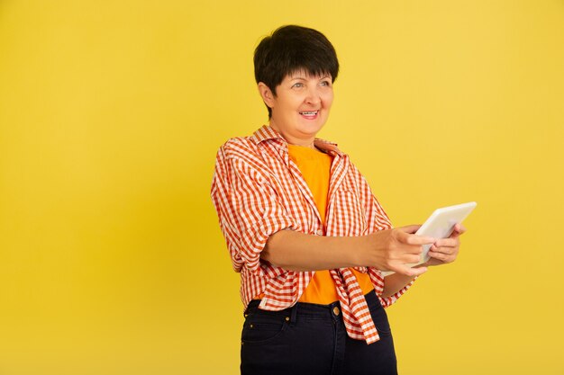 Mujer mayor aislada sobre fondo amarillo. Tecnología y concepto de estilo de vida de ancianos alegre