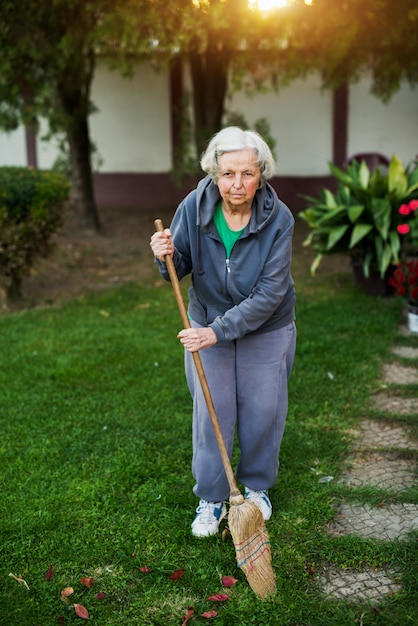 Mujer mayor alegre que sostiene la escoba en el patio trasero de la casa.