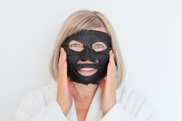 La mujer mayor aplica una máscara cosmética negra a su cara. Concepto anti edad. Rostro de mujer madura después del tratamiento de spa. Tratamiento de spa de belleza. Clínica de cirugía plástica, cosmetología, nuevo senior