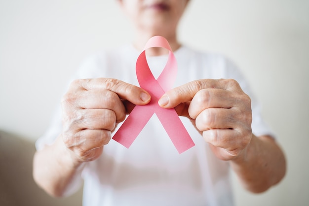 Mujer mayor apoya el día del cáncer de mama sosteniendo una cinta rosa