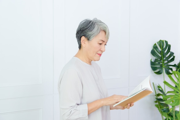 La mujer mayor de Asia está leyendo el libro sobre fondo blanco.