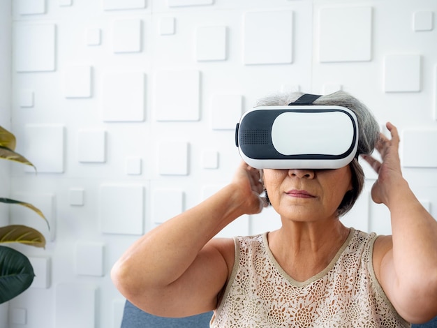 Mujer mayor asiática, la abuela con gafas VR Mujer jubilada con cabello blanco sosteniendo gafas VR en sus manos y emocionante mientras mira a través de gafas Concepto de estilo de vida de tecnología virtual de realidad