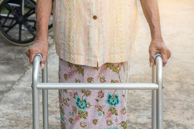 Mujer mayor asiática que se coloca con sus manos en un bastón