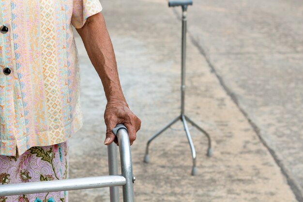 Mujer mayor asiática que se coloca con sus manos en un bastón