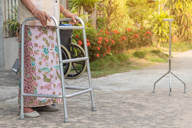 Mujer mayor asiática que se coloca con sus manos en un bastón