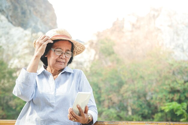 Mujer mayor asiática sosteniendo un teléfono inteligente, tomando una foto y jugando en las redes sociales, disfruta de su vida de jubilación. Concepto de comunidad de ancianos. copia espacio