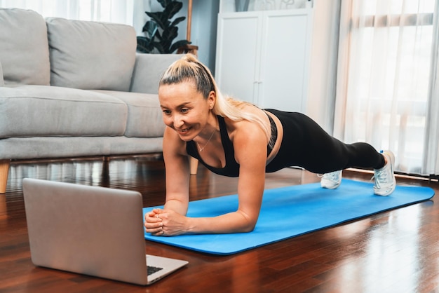 Mujer mayor atlética y deportiva haciendo planking en la alfombra de ejercicios de fitness mientras ve un video de fitness en línea en el ejercicio en casa como concepto de estilo de vida de cuerpo saludable después de la jubilación Clout