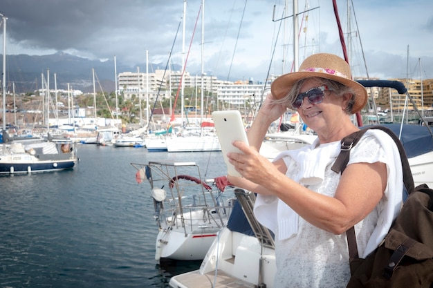 Mujer mayor atractiva con mochila. Una tableta en la mano. Barcos y puerto en el fondo