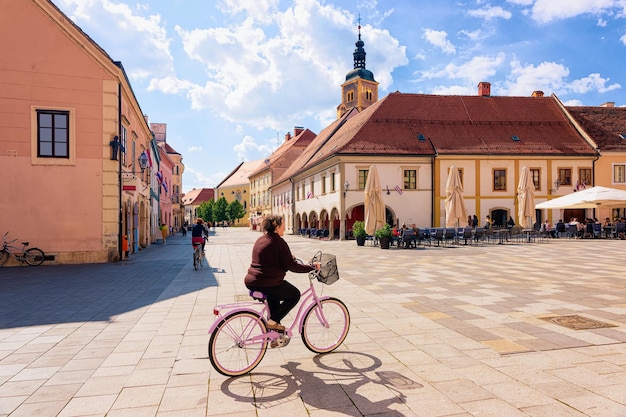 Mujer mayor en bicicleta en los cafés y restaurantes de la calle en el Ayuntamiento en la Plaza del Rey Tomislav en la ciudad vieja de Varazdin en Croacia. Paisaje urbano de la famosa ciudad croata en Europa en verano