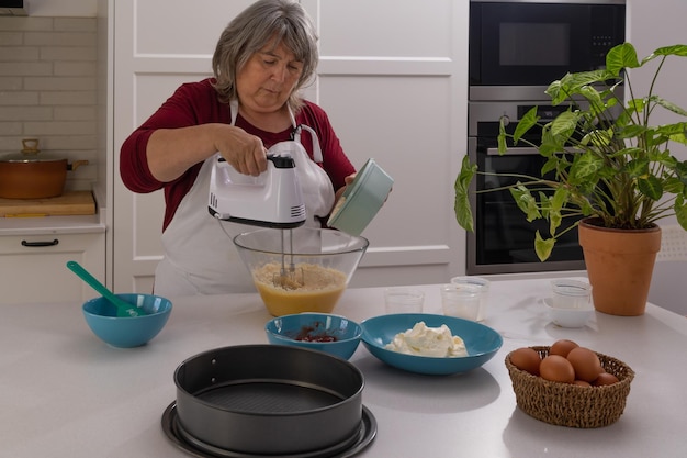 mujer mayor con cabello blanco haciendo un pastel de fresa en la cocina de su casa