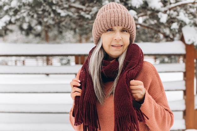 Mujer mayor con cabello gris en una bufanda de suéter de punto y sombrero en un fondo de invierno