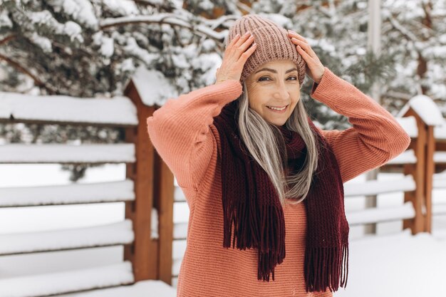 Mujer mayor con cabello gris en una bufanda de suéter de punto y sombrero en un fondo de invierno