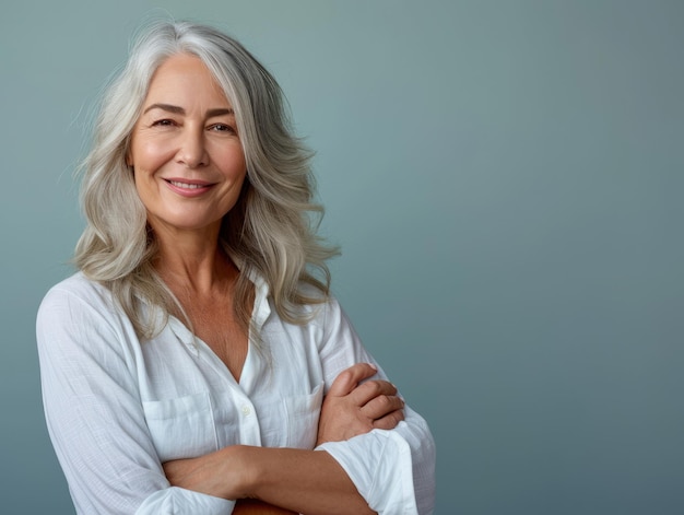 Una mujer mayor con cabello gris y camisa blanca parada con los brazos cruzados.