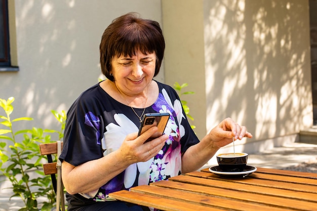 La mujer mayor en el café de la calle está usando un teléfono inteligente