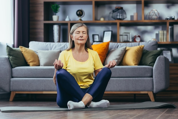 Mujer mayor canosa en casa sola estilo de vida activo yoga posición de loto y meditación