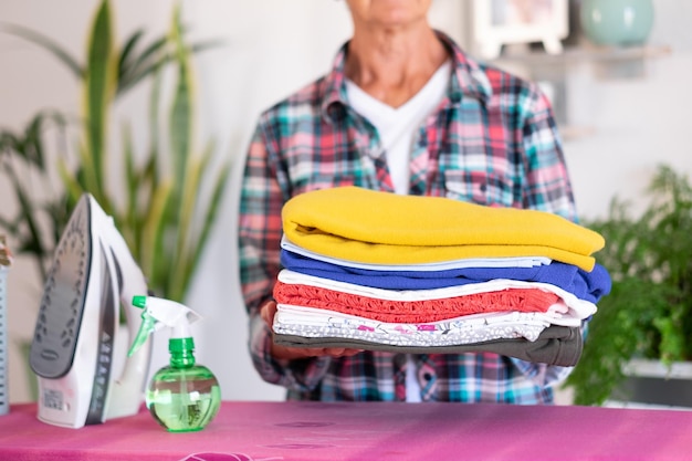 Mujer mayor caucásica en camisa a cuadros planchando ropa en casa en tabla de planchar